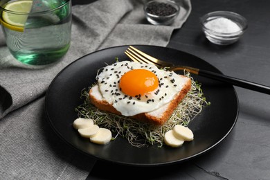 Photo of Tasty toast served with egg, cheese and microgreens on black table