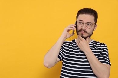 Photo of Pensive man talking on smartphone against orange background. Space for text