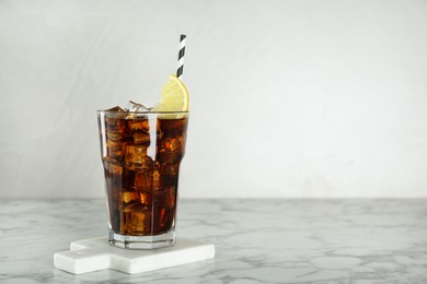 Photo of Glass of refreshing soda water with ice cubes and lemon slice on white marble table, space for text