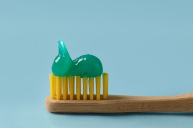 Photo of Wooden brush with toothpaste on light blue background, closeup