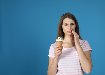 Photo of Emotional young woman with sensitive teeth and ice cream on color background. Space for text