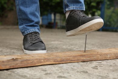 Careless man stepping on nail in wooden plank outdoors, closeup