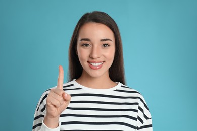 Photo of Woman showing number one with her hand on light blue background