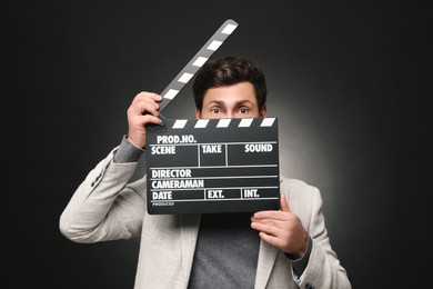 Surprised actor holding clapperboard on black background