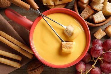 Photo of Pot of tasty cheese fondue and snacks on wooden table, flat lay