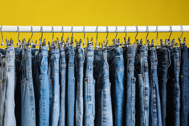 Rack with different jeans on yellow background