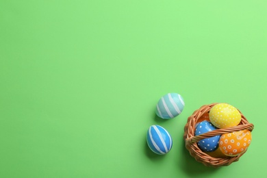 Wicker basket with painted Easter eggs on color background, top view. Space for text