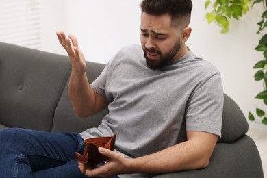 Confused man with empty wallet on sofa indoors