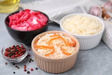 Photo of Delicious sauerkraut prepared according to different recipes and spices on light gray table, closeup