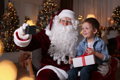 Photo of Santa Claus and little boy taking selfie in room decorated for Christmas