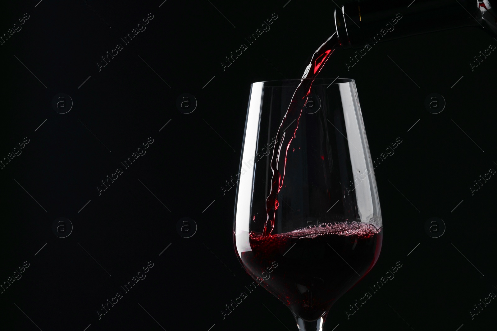 Photo of Pouring red wine into glass against black background, closeup. Space for text