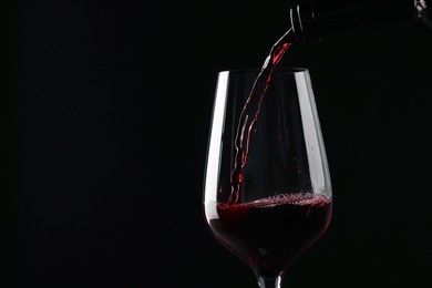 Pouring red wine into glass against black background, closeup. Space for text