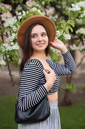 Beautiful woman in hat near blossoming tree on spring day