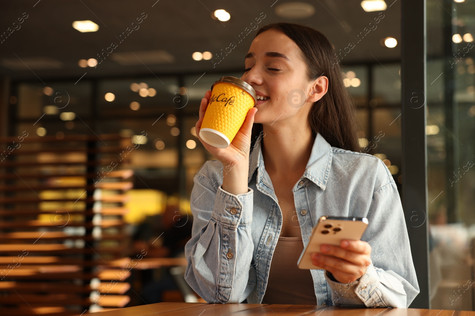 Photo of Lviv, Ukraine - September 26, 2023: Woman with hot McDonald's drink and smartphone in cafe