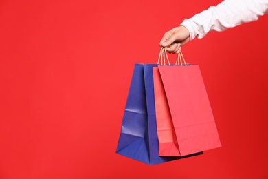 Young man with paper bags on red background, closeup. Space for text