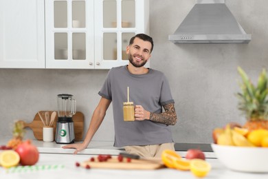 Photo of Handsome man with delicious smoothie in kitchen