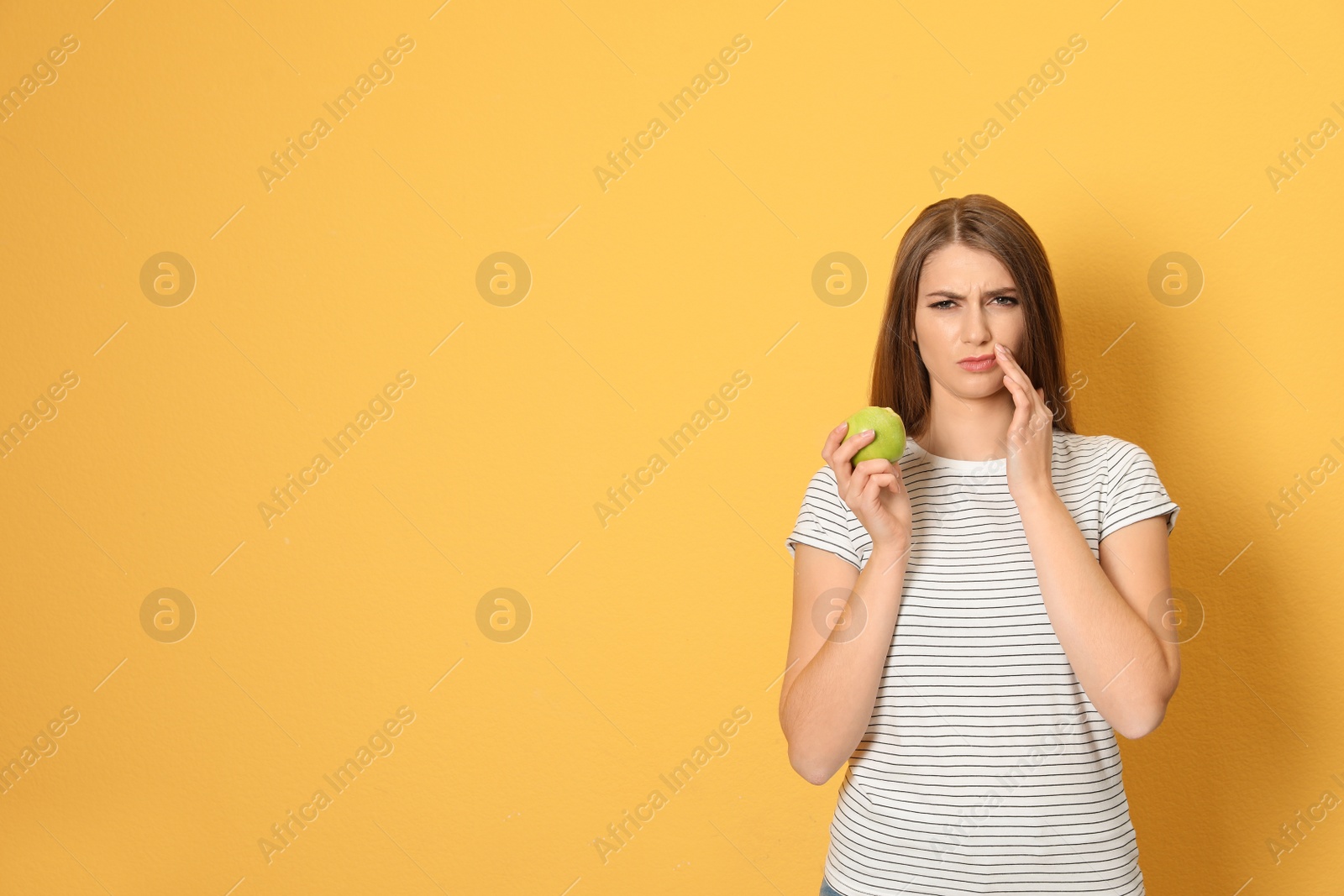 Photo of Emotional young woman with sensitive teeth and apple on color background. Space for text