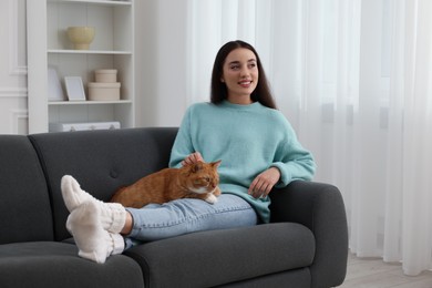 Photo of Beautiful woman petting cute cat on sofa at home