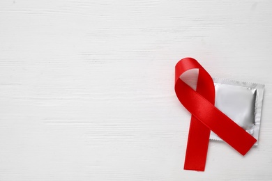 Photo of Red ribbon and condom on white wooden background, flat lay with space for text. AIDS disease awareness