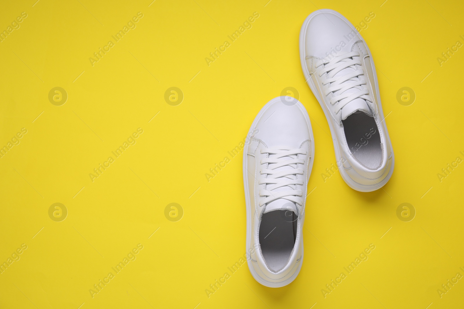 Photo of Pair of stylish white sneakers on yellow background, top view. Space for text