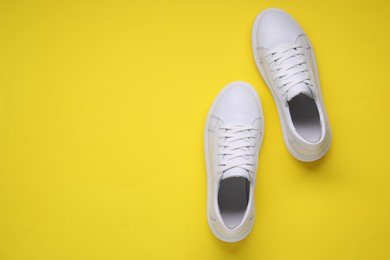 Photo of Pair of stylish white sneakers on yellow background, top view. Space for text