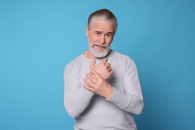 Photo of Senior man suffering from pain in hands on light blue background. Arthritis symptoms