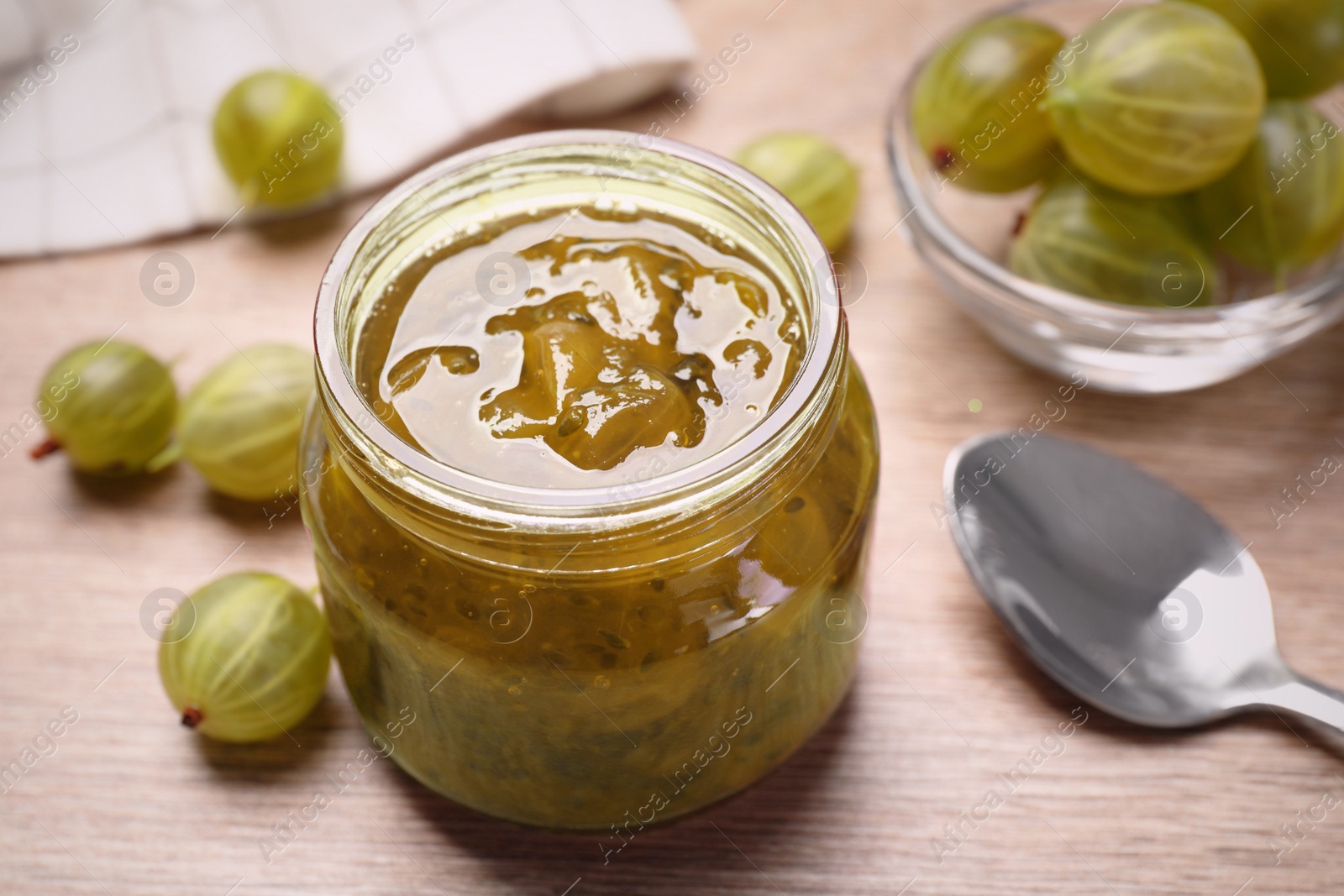 Photo of Jar of delicious gooseberry jam and fresh berries on wooden table, closeup