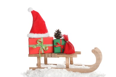 Photo of Wooden sleigh with Christmas gift boxes, Santa hat and artificial snow on white background