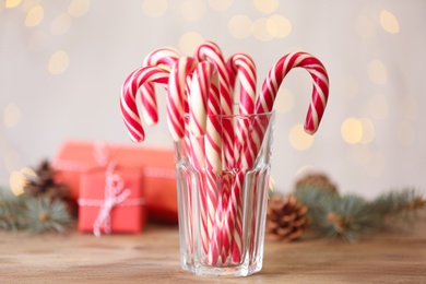 Photo of Christmas candy canes on wooden table against blurred lights