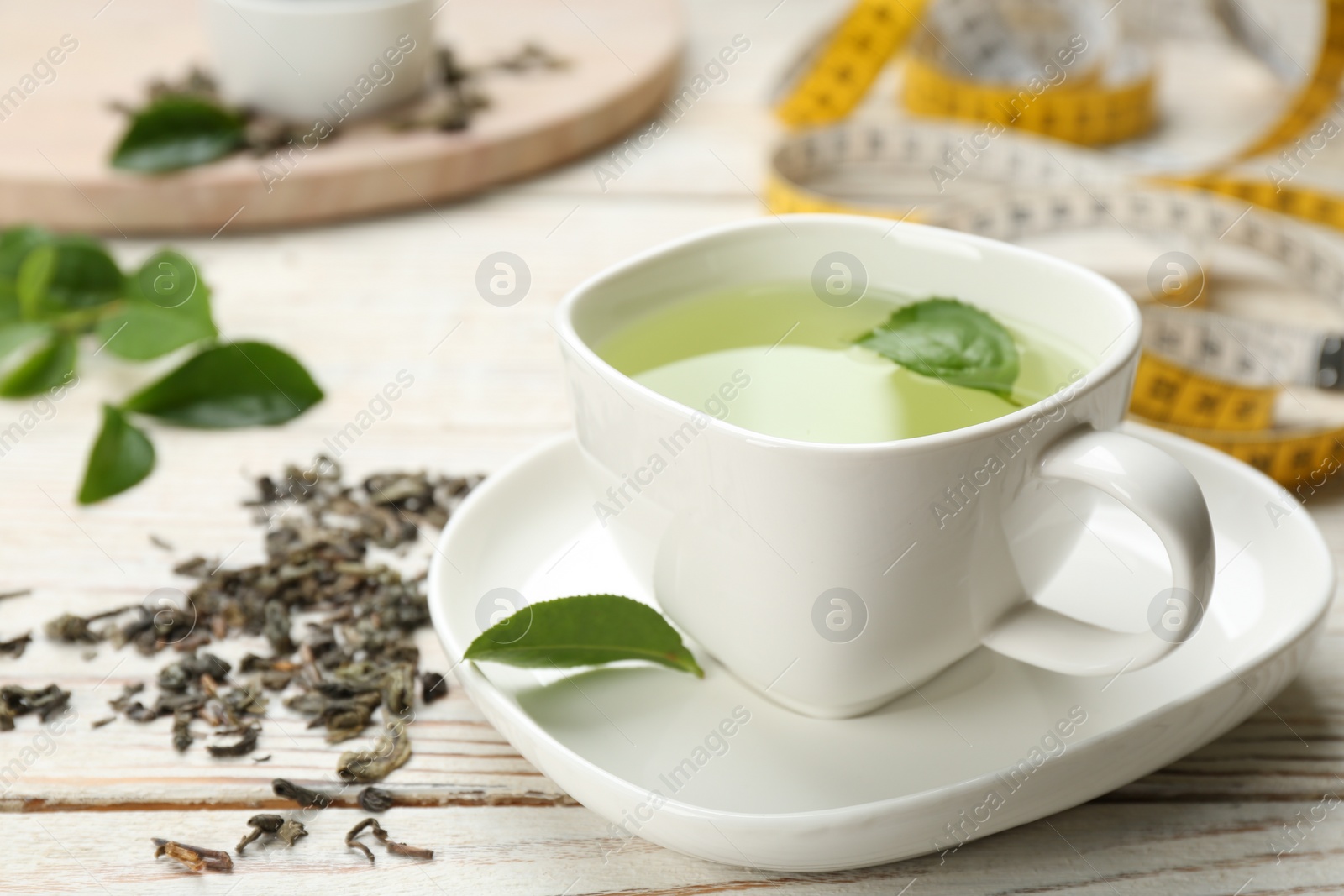 Photo of Cup of diet herbal tea and measuring tape on white wooden table