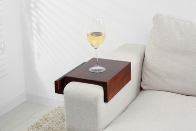 Glass of white wine on sofa with wooden armrest table in room. Interior element