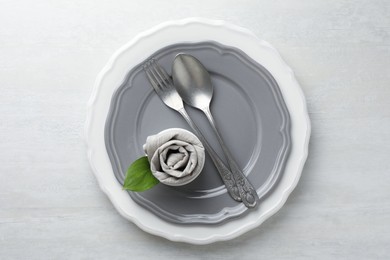 Photo of Stylish setting with cutlery, napkin, leaf and plates on light textured table, top view