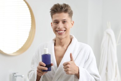 Photo of Young man with mouthwash showing thumbs up in bathroom