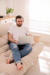 Photo of Man with laptop and headphones sitting on sofa at home