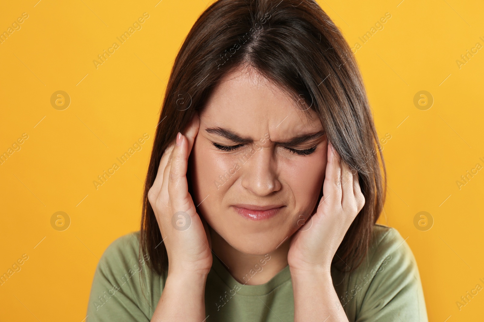 Photo of Young woman suffering from migraine on yellow background