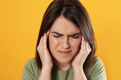 Young woman suffering from migraine on yellow background