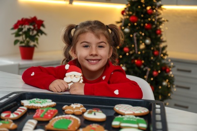 Cute little girl with freshly baked Christmas gingerbread cookie at table indoors