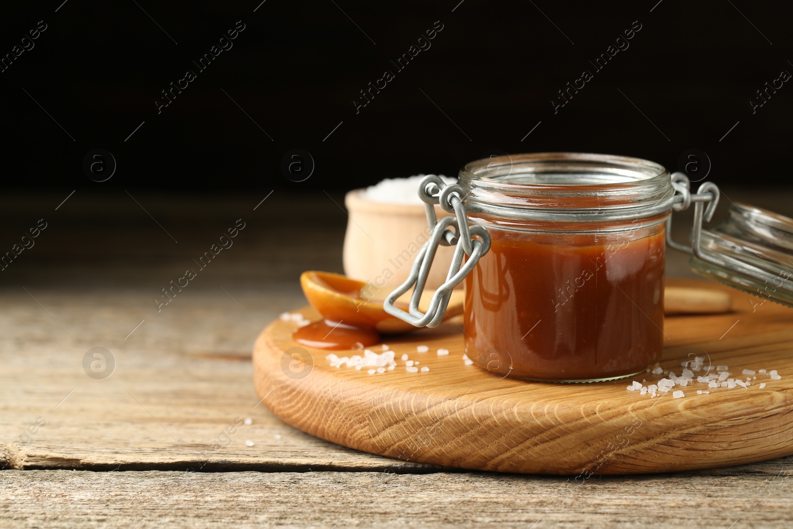 Photo of Tasty salted caramel in jar and salt on wooden table, space for text