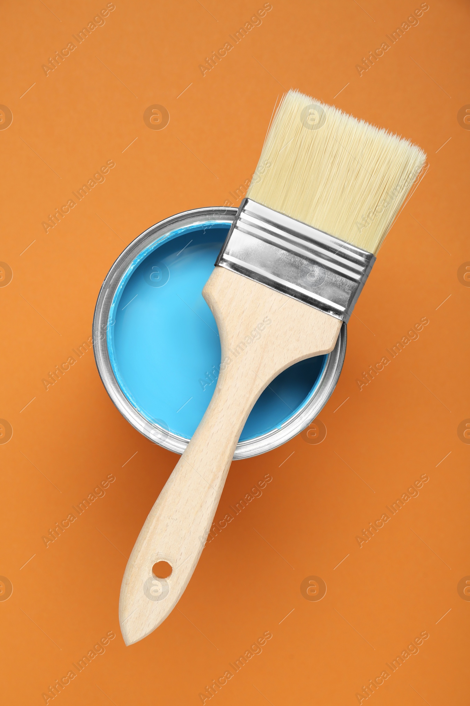 Photo of Can of light blue paint with brush on pale orange background, top view