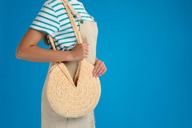 Young woman with stylish straw bag on light blue background, closeup. Space for text