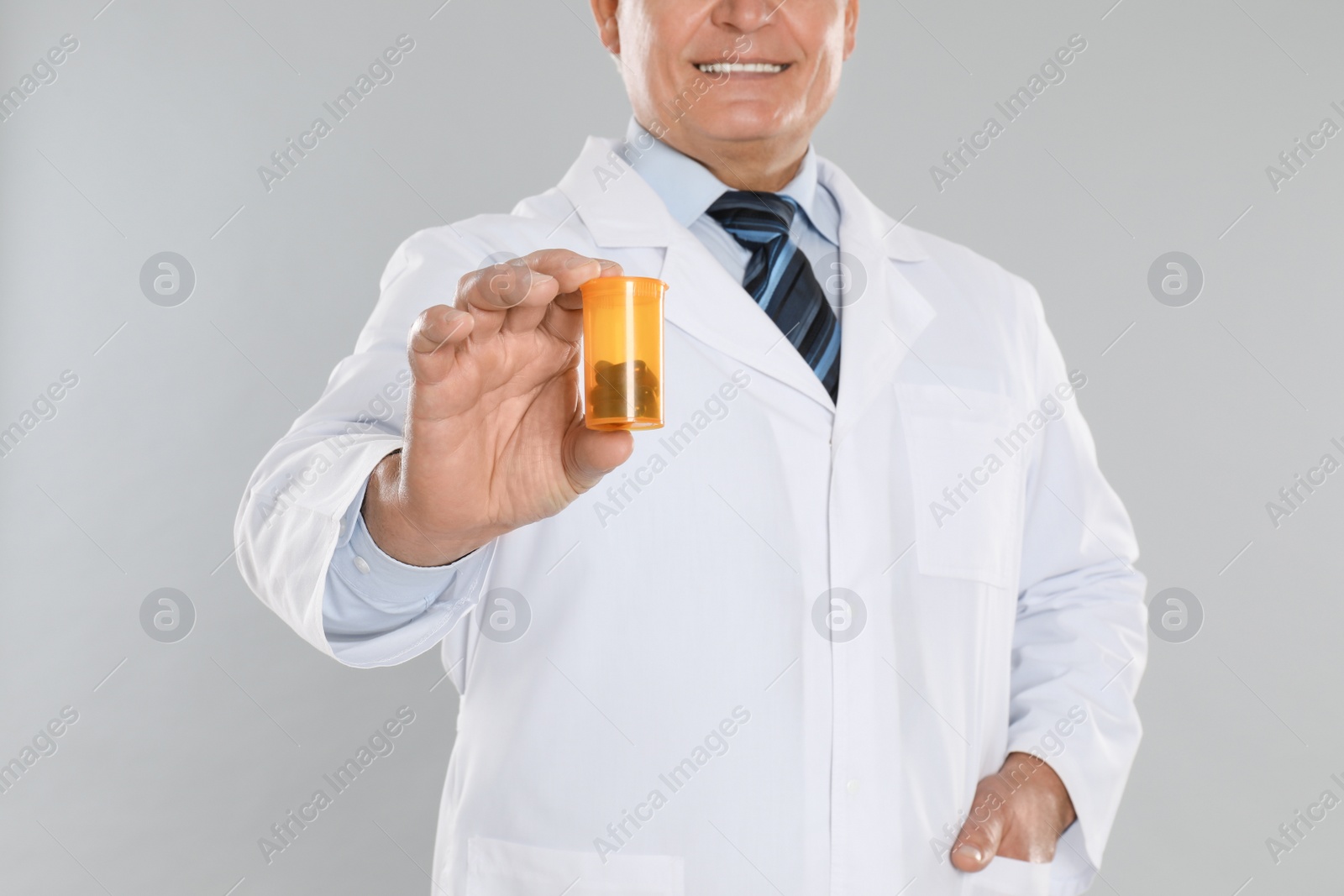 Photo of Senior pharmacist with pills on light grey background, closeup