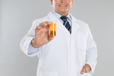 Photo of Senior pharmacist with pills on light grey background, closeup