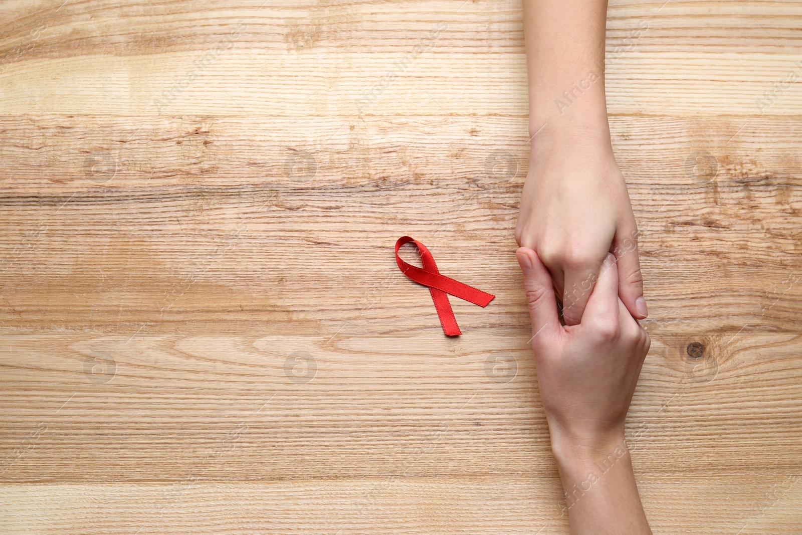 Photo of Women holding hands near red awareness ribbon on wooden background, top view with space for text. World AIDS disease day