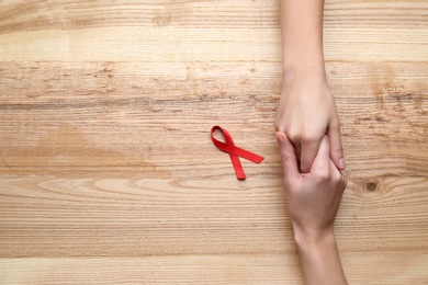 Photo of Women holding hands near red awareness ribbon on wooden background, top view with space for text. World AIDS disease day