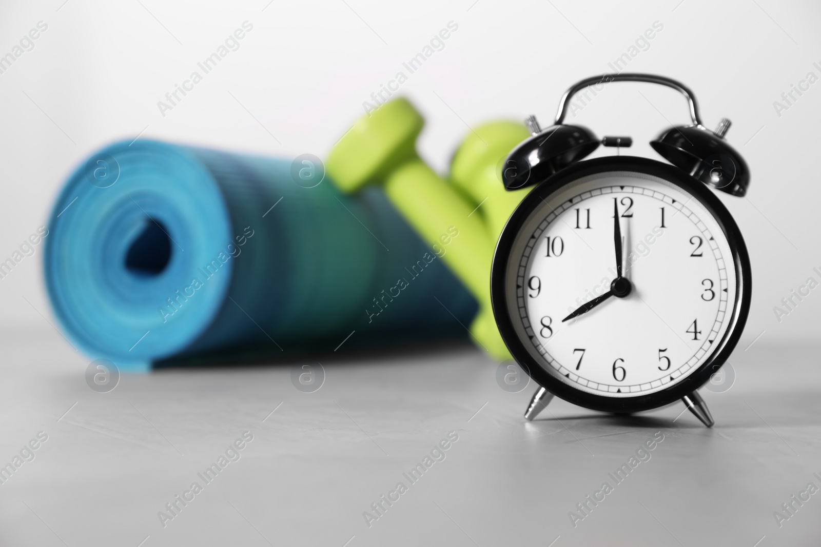 Photo of Alarm clock, yoga mat and dumbbells on grey background. Morning exercise