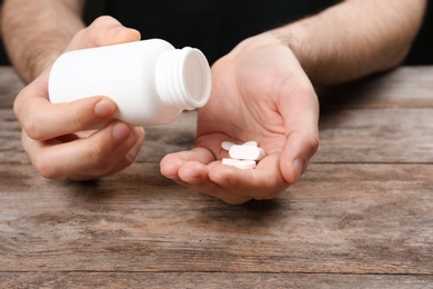 Man pouring pills out of bottle into hand at table, closeup