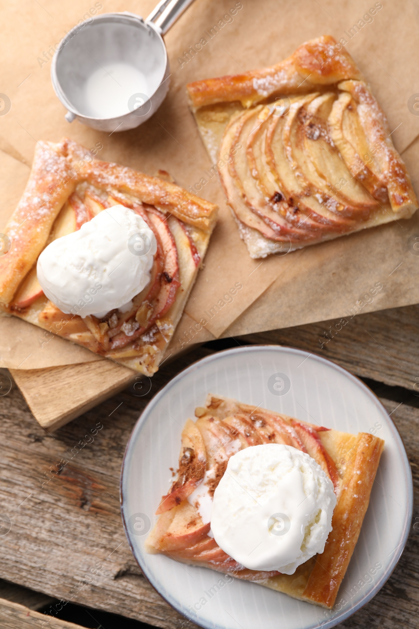 Photo of Pieces of freshly baked apple pie served with ice cream on wooden table, flat lay