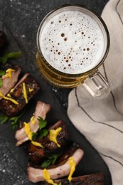 Photo of Mug with beer and delicious grilled ribs on dark grey textured table, flat lay