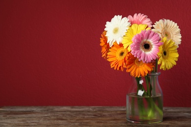 Photo of Bouquet of beautiful bright gerbera flowers in vase on wooden table against color background. Space for text