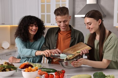 Photo of Friends cooking healthy vegetarian meal at white marble table in kitchen